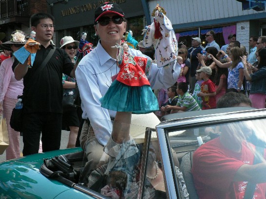 駐加拿大代表李大維伉儷參加加拿大國際偶戲節 (Puppets Up! Festival) 遊行活動，手持台灣布袋戲與參觀遊行民眾親切互動。