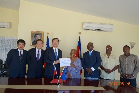 黃大使再求(左3)、賈參事彝(左2)、顏參事嘉良(左1)與海地「Marmelade地區整體永續發展基金會」（FONDDIM）董事長Marie Claude CALVIN(右4)及該基金會副董事長Jacques Renand CHERDUVILLE大使(右3)在館舉行援贈儀式合影。