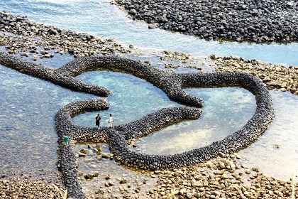 台湾海峡に浮かぶ澎湖群島の南端に位置するのが七美です。澎湖県の県庁所在地である馬公から船で約1時間。美しい海岸で知られる小さな島です。この島は「雙心石滬」という景観で知られています。これは玄武岩とサンゴ礁で築かれた伝統的な石垣で、潮の干満を利用した古来の漁法でもあります。満潮時には潮の流れによって石垣の内側に多くの魚たちが入ってきますが、干潮時を迎えると出られなくなるという仕組みです。かつては澎湖各地で見られたと言いますが、現在はその数を減らしており、貴重な存在となっています。その風貌が2個のハートが連なっているように見えることから、多くのカップルが訪れるようになり、今や七美を代表する観光スポットになっています。まだまだ手つかずの自然が残る澎湖の離島。ちょっと足をのばしてみる価値はありそうです。