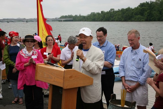 駐美代表處袁代表健生於2009年5月16日舉行之第八屆華府龍舟賽點睛儀式中致詞。袁代表夫人（左二）、華盛頓特區市議會議長葛雷（Vincent Gray）（右三）、市議員伊凡斯（Jack Evans）（右二）。
