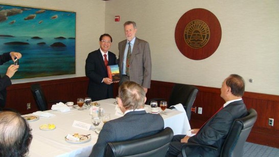 三一大學校長Dennis Ahlburg與廖東周處長交換禮物並合影，右為聖安東尼僑務委員胡啟年