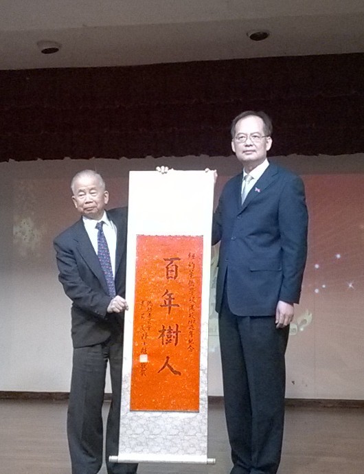 章文樑大使（右）頒發「百年樹人」的賀軸給華僑學校，由黃炯常校長（左）表接受。