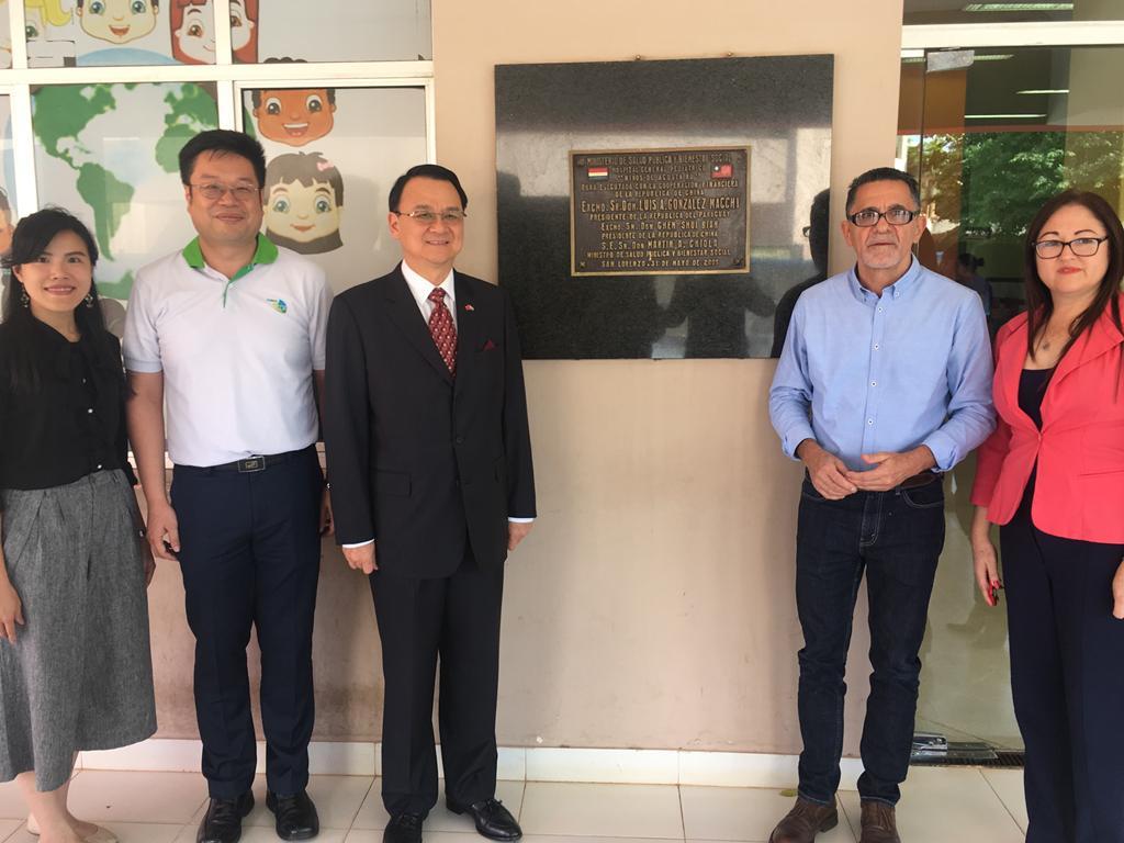 中華民國駐巴拉圭周麟大使於108年1月29日偕駐館及技術團同仁參訪Niños de Acosta Ñu兒童醫院，院長Pio Alfieri偕行政主任Angélica Sanabria等人陪同參觀院區，介紹該院行政及資訊系統作業。圖為駐巴拉圭周大使麟(左三)與Niños de Acosta Ñu兒童醫院院長Pio Alfieri(右二)等人於醫院落成紀念牌前合影留念。
