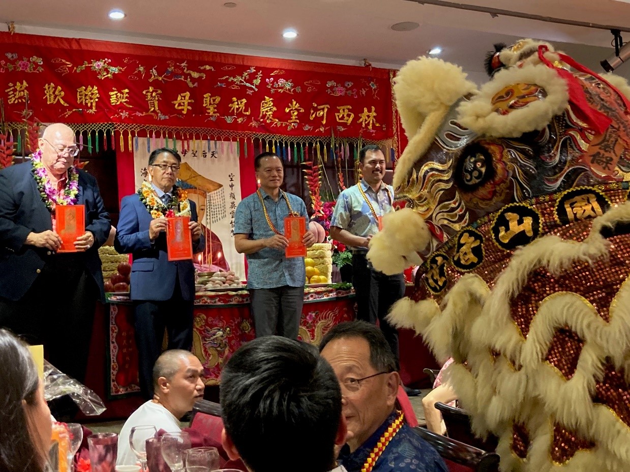 2023年5月21日林暉程處長與林西河堂會長譚偉添(左二)˴副會長林子安(左一)及檀香山市議員Tyler Dos Santos-Tam (右一)共同於慶祝聖母寶誕暨成立134週年晚宴中接受舞獅祝賀