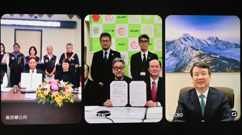 李逸洋・駐日代表（写真右スクリーン）が立ち会うなか、梁光明・花蓮県萬栄郷長（左スクリーン前右２）と遠藤桂一・北海道平取町長（中央スクリーン前右２）が友好交流協定に調印。