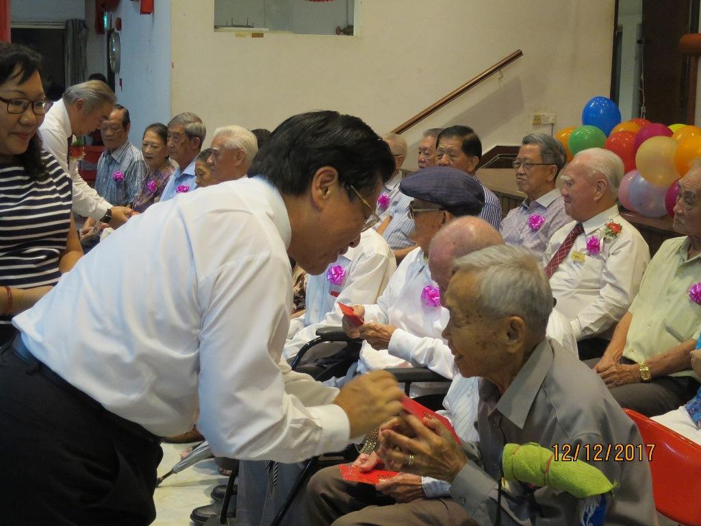 梁代表（前方站立側身）致贈敬老紅包給每一位耆老，該公會李主席志遠隨後發贈鳳梨酥禮盒。(106年12月12日)